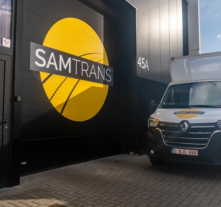 Meubelwagen van SamTrans naast het magazijn van express transport SamTrans met duidelijk zichtbaar logo